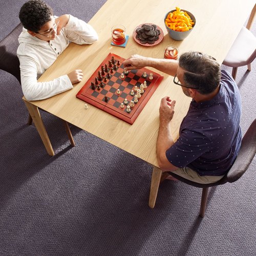 father and son playing chess and eating snack on brown table in a living room with gray carpet from Carter Carpets & Vinyl in Temperance, MI